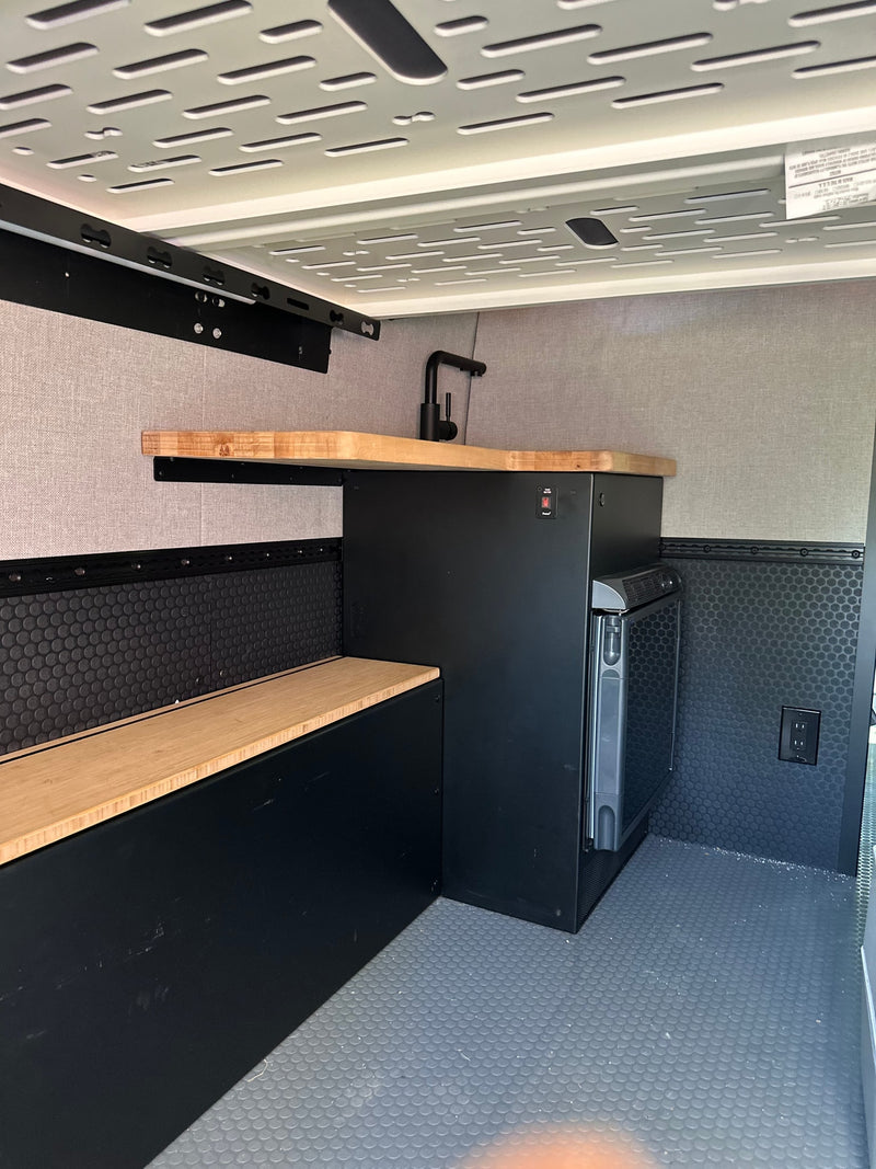 Compact RV rental interior featuring a kitchenette with wood counter, sink, fridge, and built-in bench. — photo 12