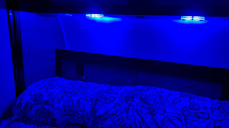 A vibrant blue light illuminates the sleeping area of an RV rental, showing a bed with patterned bedding and overhead lamps. — photo 13