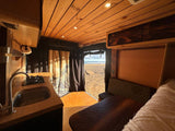 This cozy **RV rental** features a warm wood interior, kitchen, and a stunning beach view, perfect for **van life** adventures by the **sea**.