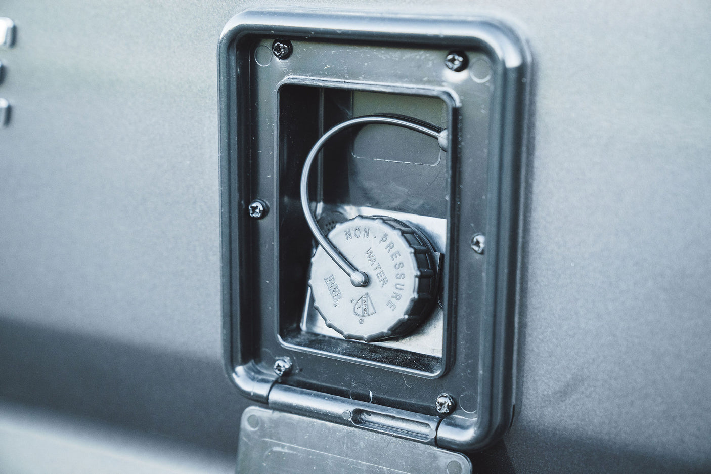 RV rental's non-pressure water fill port with a tethered cap, crucial for clean water supply during camping and travel.