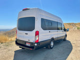 White Ford Transit RV rental van parked on a dirt trail, ready for outdoor adventure in a dry, hilly landscape.