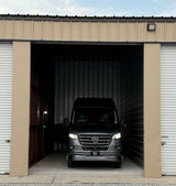Grey Mercedes-Benz Sprinter RV rental van parked in a large storage unit with its lights on, ready for use.