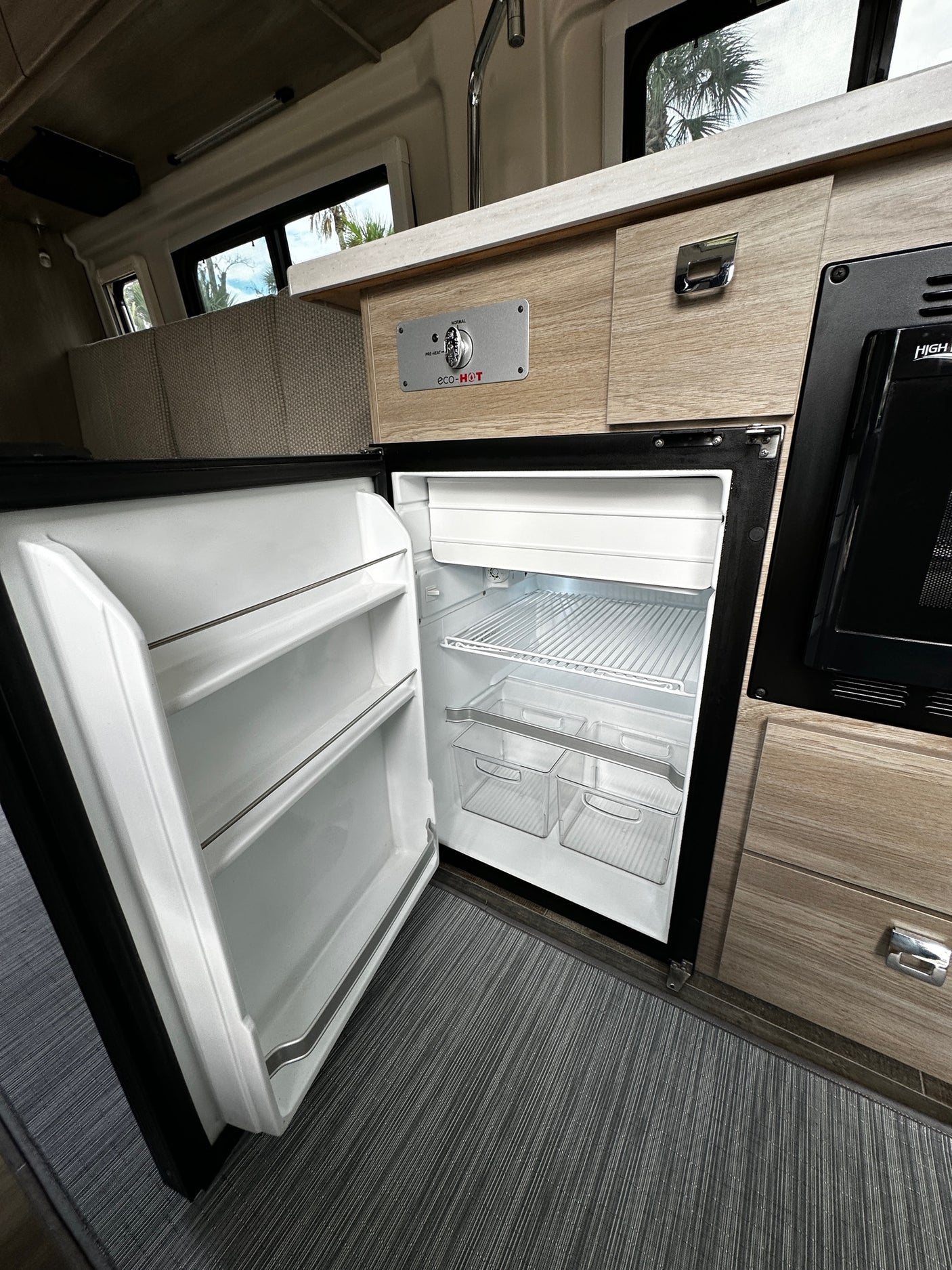 Inside an RV rental: a clean, open refrigerator, microwave, and wood-paneled interior. Ready for your adventure.
