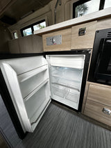 Inside an RV rental: a clean, open refrigerator, microwave, and wood-paneled interior. Ready for your adventure.
