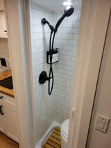 Modern RV rental shower with white subway tiles, black fixtures, wooden floor, and toilet. A compact and functional bathroom.