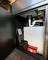 This RV rental's utility compartment houses sink plumbing, a water tank, folded stool, and a first-aid kit for convenience.