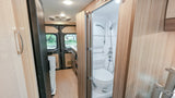 Compact RV rental interior: Bathroom with shower & toilet, leading to kitchen & rear view. Perfect for adventures!
