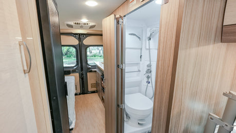 Compact RV rental interior: Bathroom with shower & toilet, leading to kitchen & rear view. Perfect for adventures!