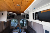 Cozy RV rental dining area with a wooden ceiling, open white cabinets, set table with plates & cups, and scenic views.