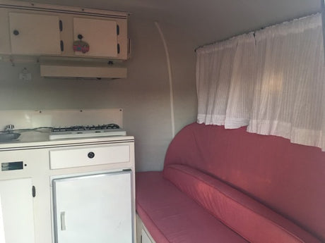RV rental interior: compact kitchen (stove, sink, fridge) & red cushioned bench for travel comfort.