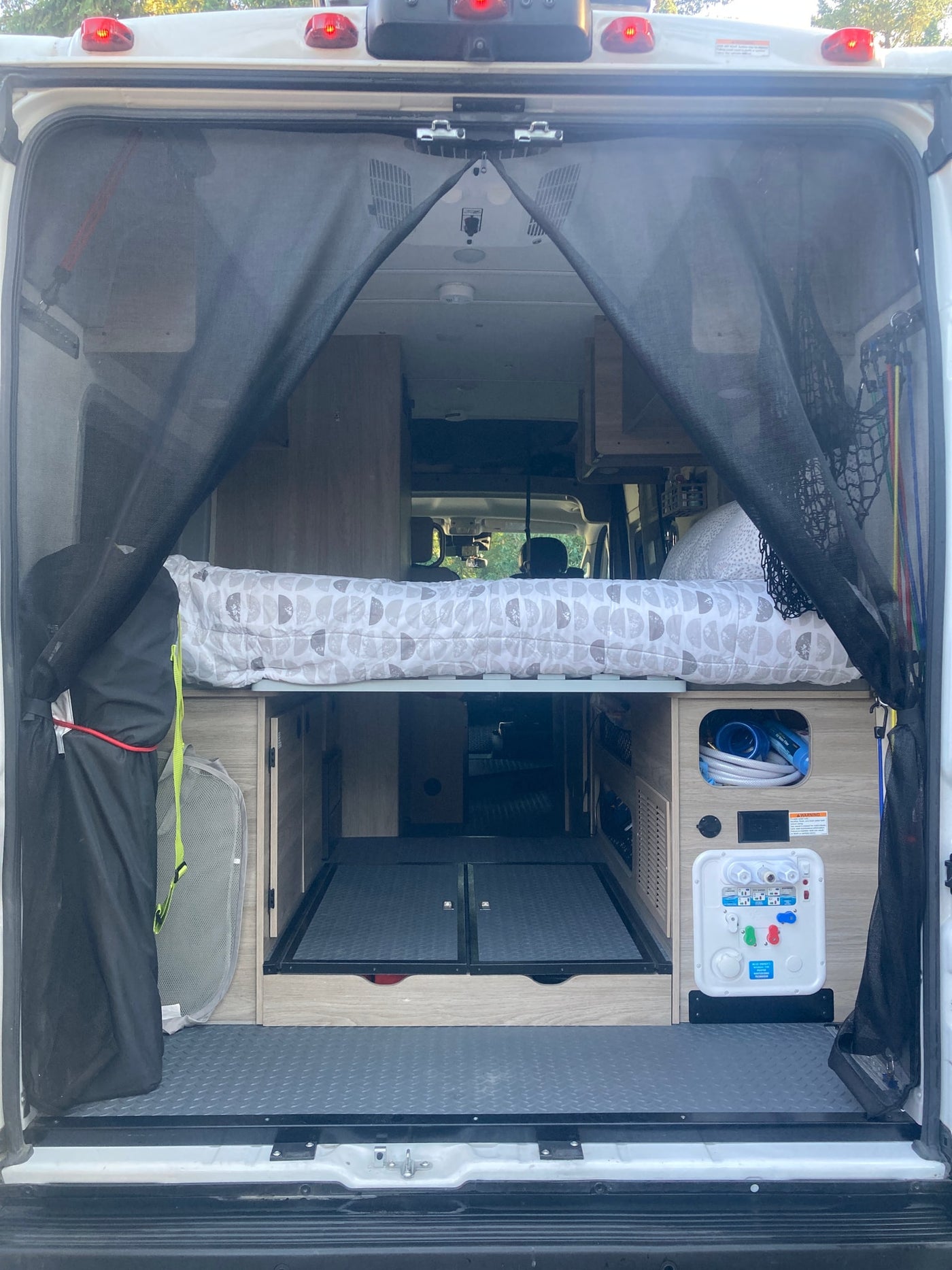 Rear view of an rv rental camper van interior. Shows comfy bed, organized storage, and water utility panel for road trip van life. — photo 15