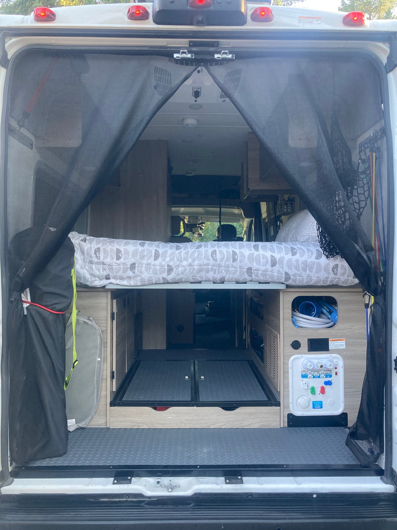 Rear view of an rv rental camper van interior. Shows comfy bed, organized storage, and water utility panel for road trip van life. — photo 15