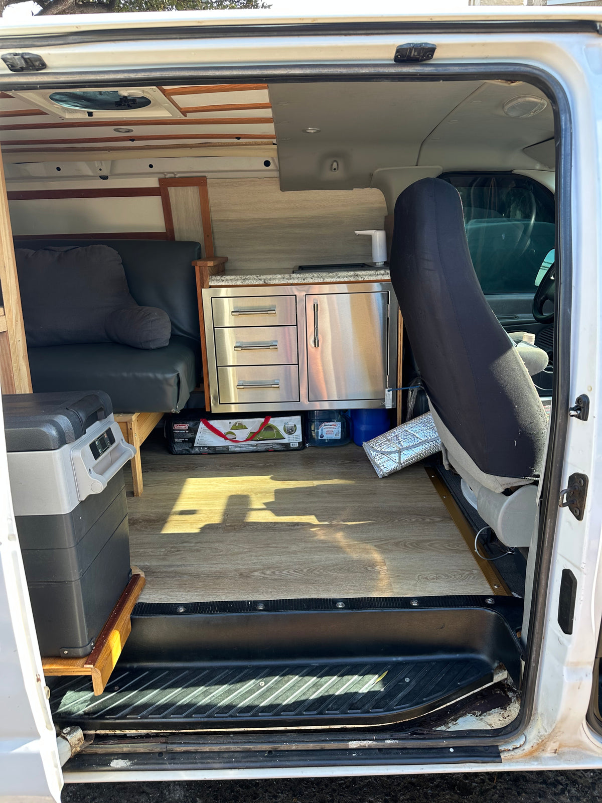RV rental camper van interior. Features a compact kitchenette, convertible seating/bed, and portable fridge for travel. — photo 10