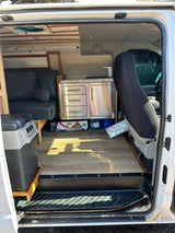 RV rental camper van interior. Features a compact kitchenette, convertible seating/bed, and portable fridge for travel.