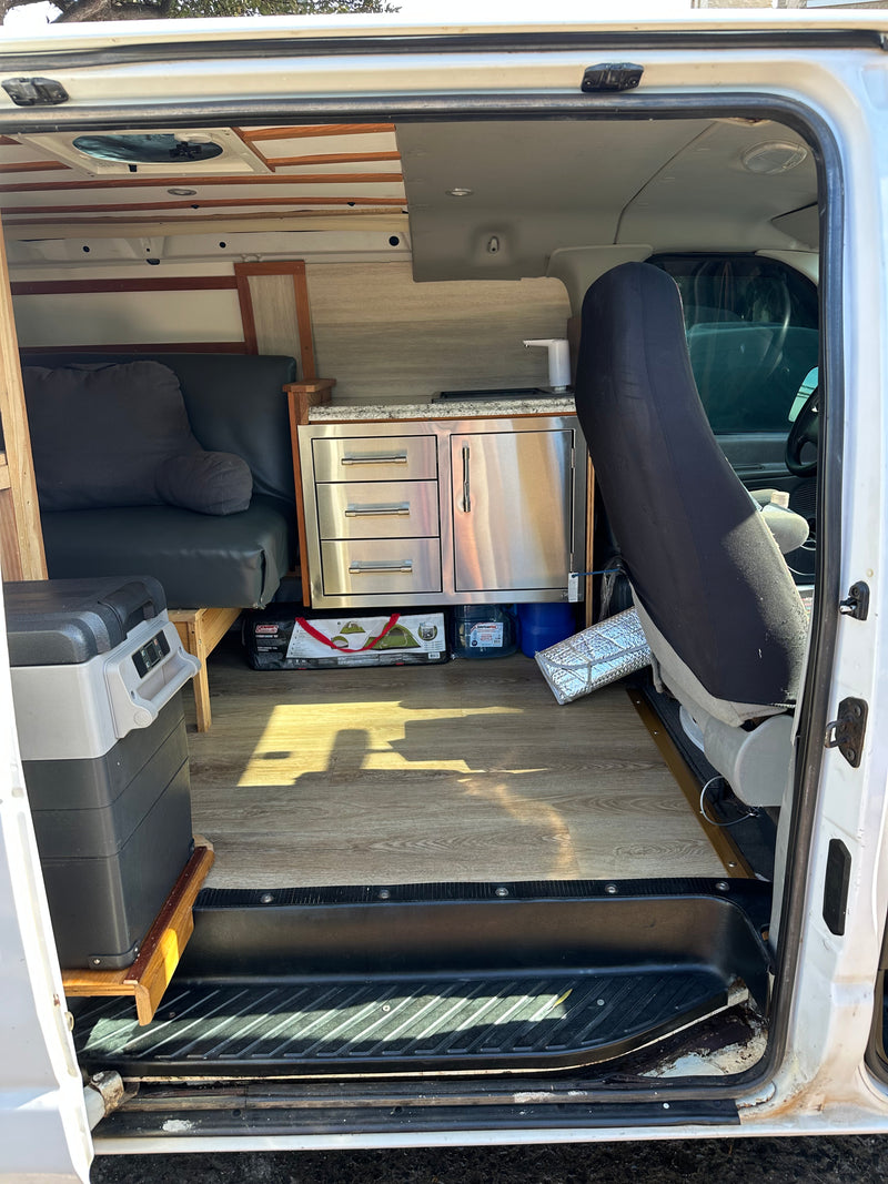 RV rental camper van interior. Features a compact kitchenette, convertible seating/bed, and portable fridge for travel. — photo 10