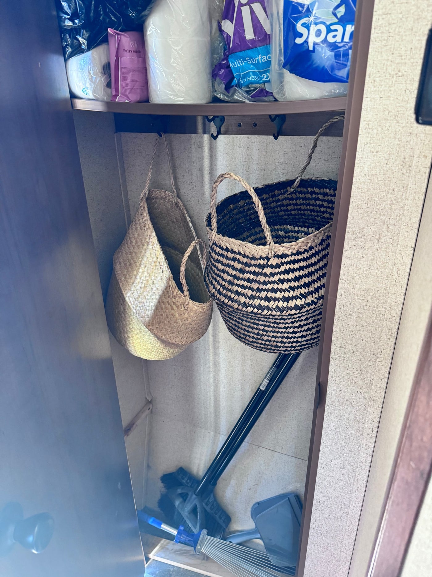 RV rental closet showing practical storage: paper products, cleaning supplies, and woven baskets with hooks for organization. — photo 7