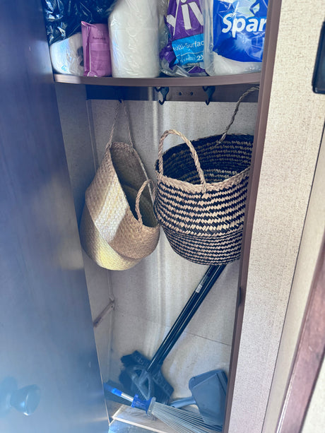 RV rental closet showing practical storage: paper products, cleaning supplies, and woven baskets with hooks for organization.