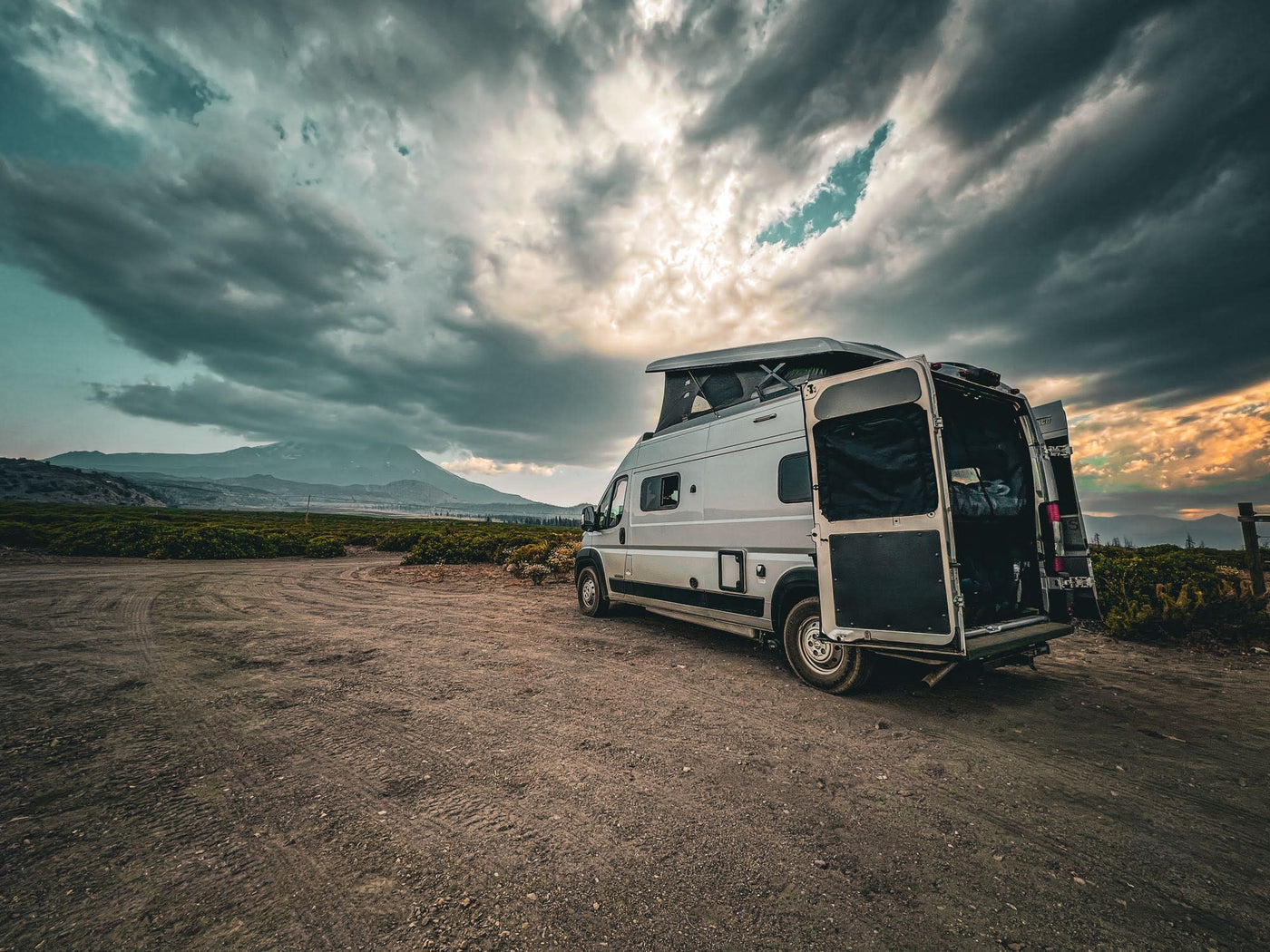  and blue mountains in the distance. Ideal for scenic road trips.|Silver RV rental camper van parked on a scenic mountain road under a clear blue sky — photo 7