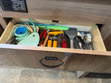 Compact kitchen drawer in an RV rental, stocked with essential utensils, measuring cups, and cutlery for your trip.