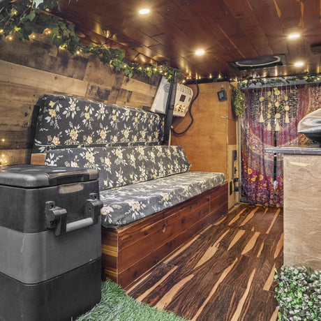 This RV rental's cozy interior features floral bench seating, wooden walls & ceiling, and ambient string lights.