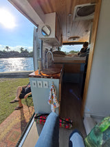 Enjoying a serene RV rental setup with the door open to a sunny waterfront view, blending indoor comfort with outdoor beauty.