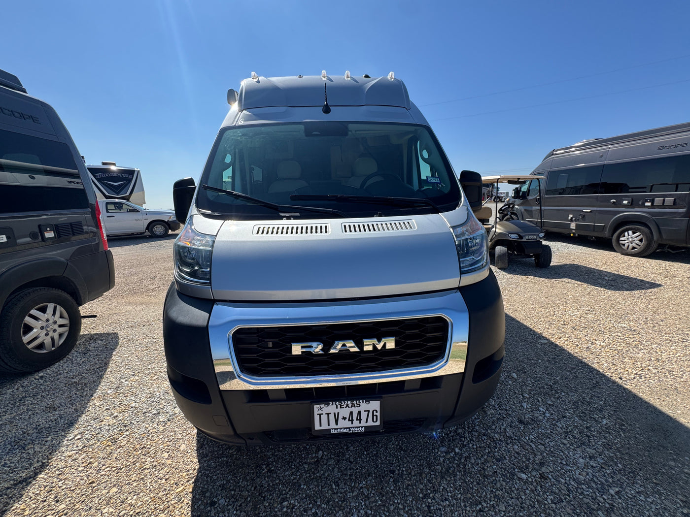 Front view of a silver Ram ProMaster rv rental van parked on a sunny gravel lot, with other RVs and a golf cart visible. — photo 3