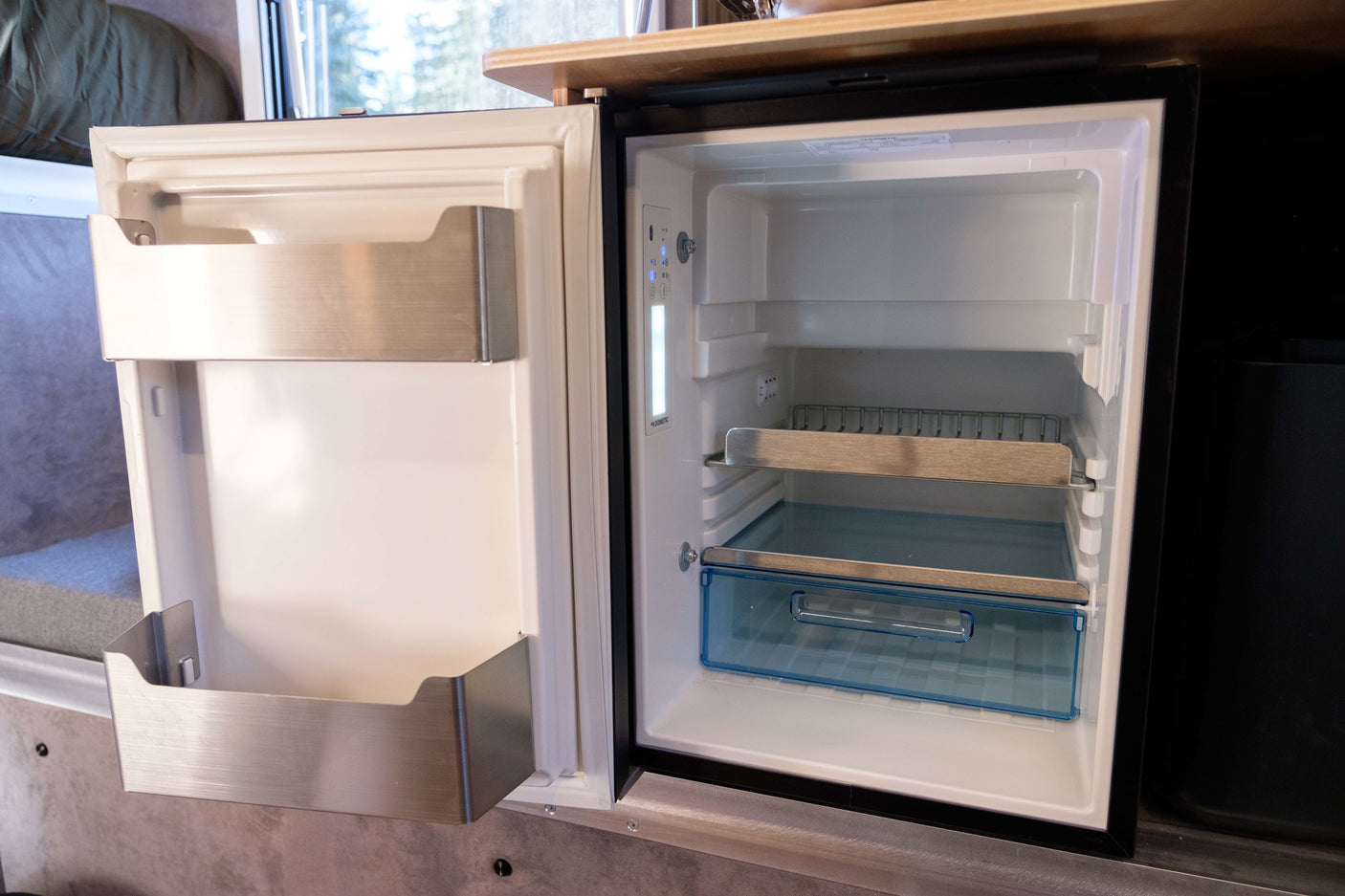Open, compact fridge in an RV rental, revealing empty shelves & door bins. Features include a control panel & built-in storage.