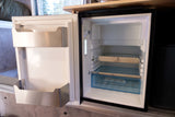 Open, compact fridge in an RV rental, revealing empty shelves & door bins. Features include a control panel & built-in storage.