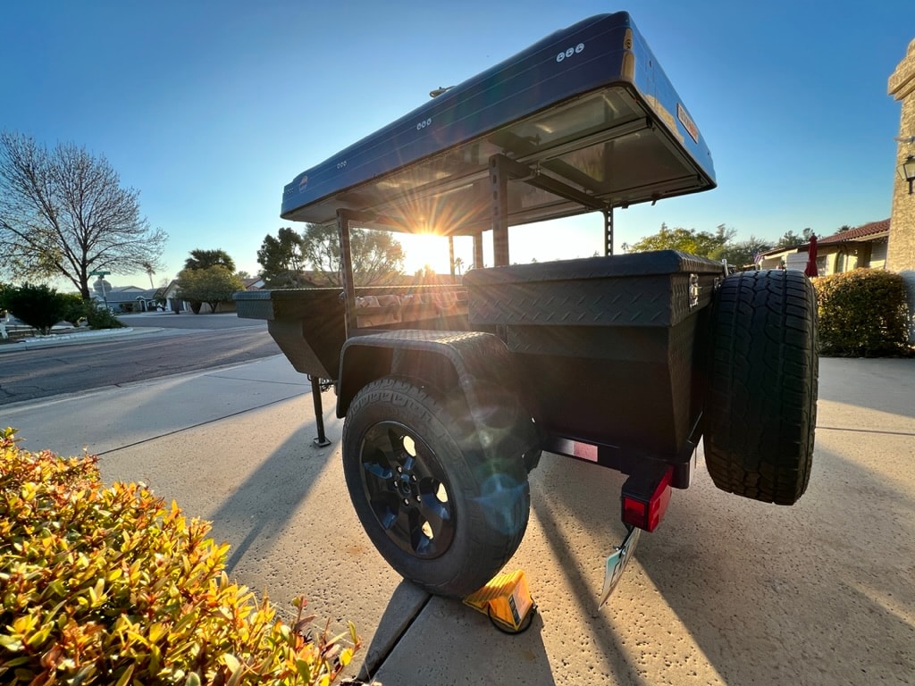 Sun-drenched black overland trailer with rooftop tent, ready for your RV rental getaway. Spare tire visible. — photo 13