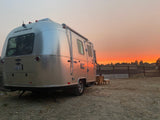An Airstream rv rental gleams under a dramatic orange sunset, inviting outdoor relaxation and travel adventures.