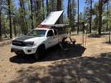 Overland-equipped Toyota Tacoma truck with pop-top camper & awning in a pine forest. Great for an rv rental adventure.
