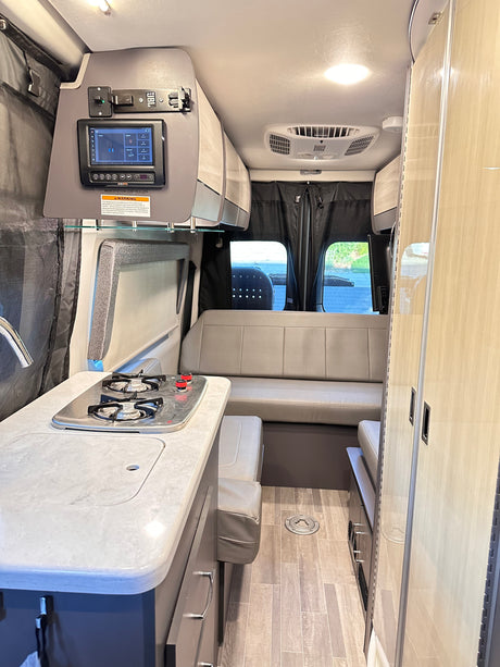 Spacious rv rental interior featuring a modern kitchen with stovetop, integrated control panel, and comfortable dinette.
