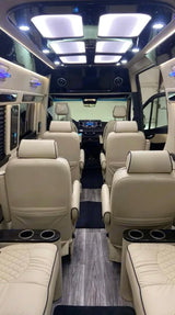 Spacious luxury RV rental interior featuring plush cream captain's chairs, elegant ceiling lights, and modern wood flooring.