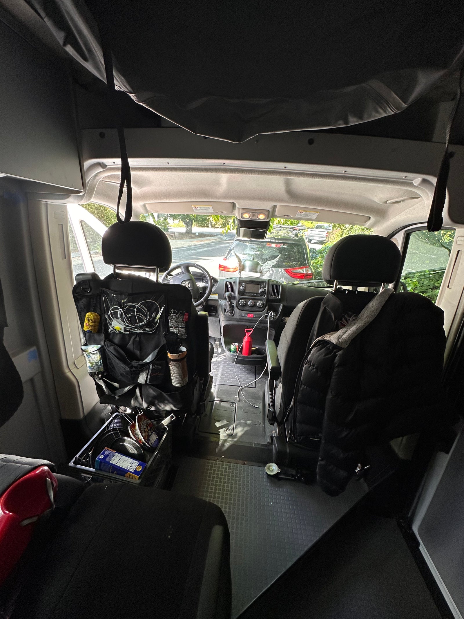 View into the front of an rv rental van, showcasing driver's area, passenger seat, and behind-seat organizers.