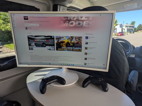 Inside an rv rental, a large monitor displays Asphalt 8 on Microsoft Store. Two Xbox controllers are ready for mobile gaming.