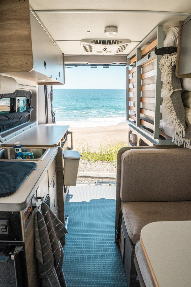 Inside an RV rental, enjoy ocean views from the back. Features a kitchen, seating area, and cozy mobile living space. — photo 4