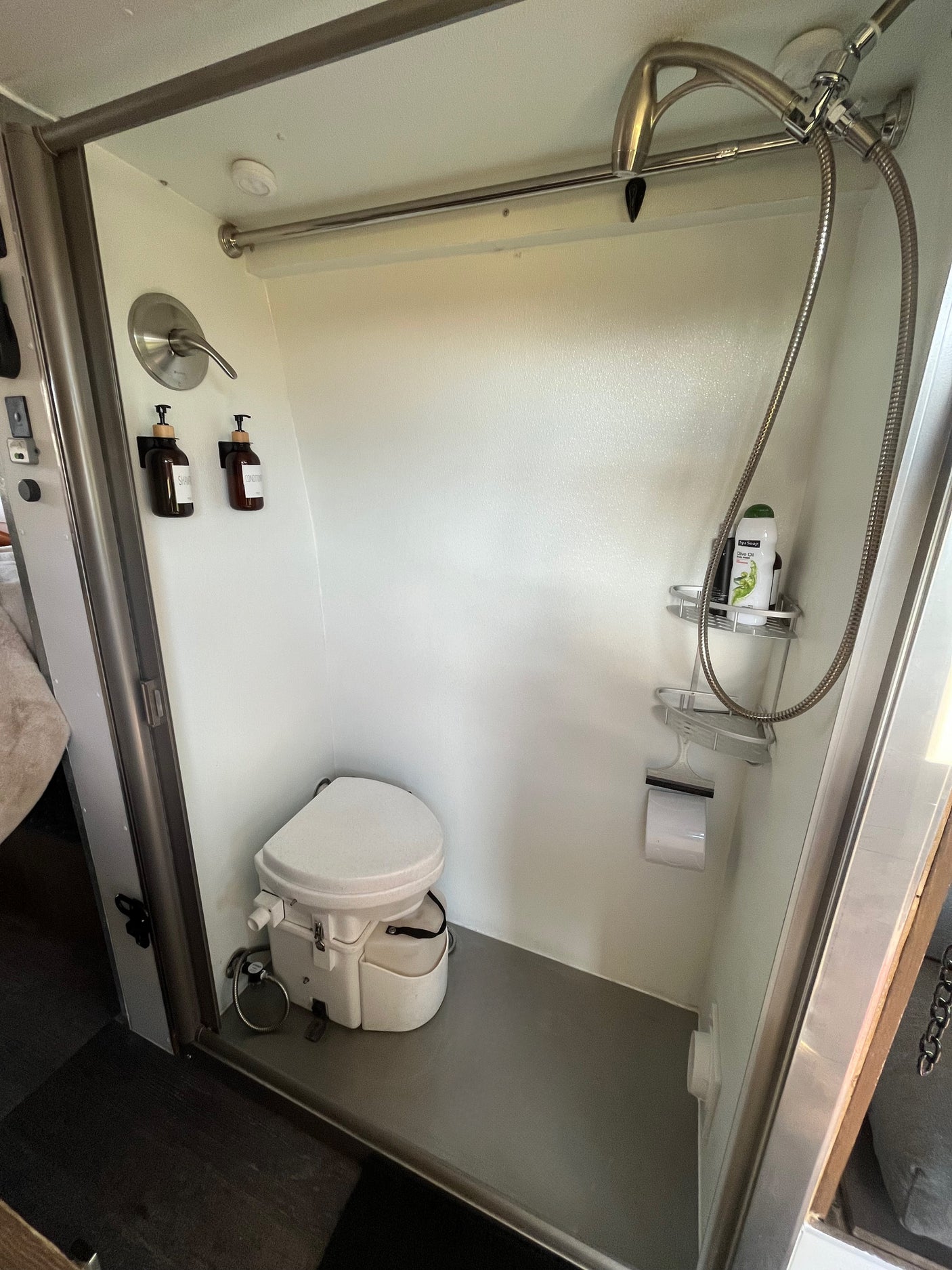 RV rental compact bathroom showing a white composting toilet, a shower with wall-mounted toiletries.