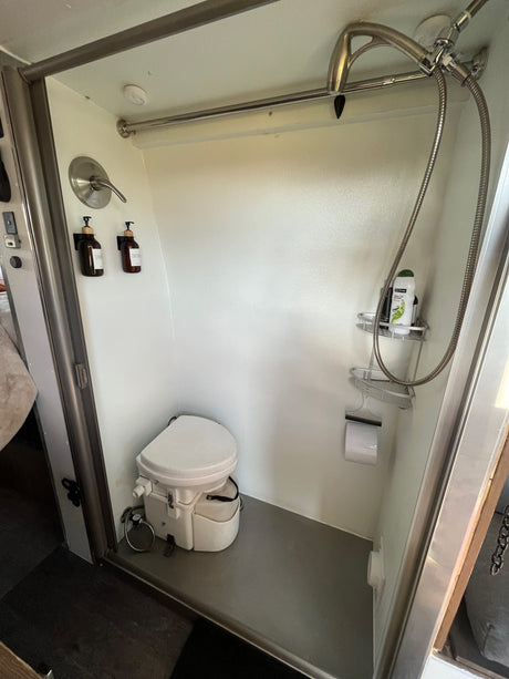 RV rental compact bathroom showing a white composting toilet, a shower with wall-mounted toiletries.