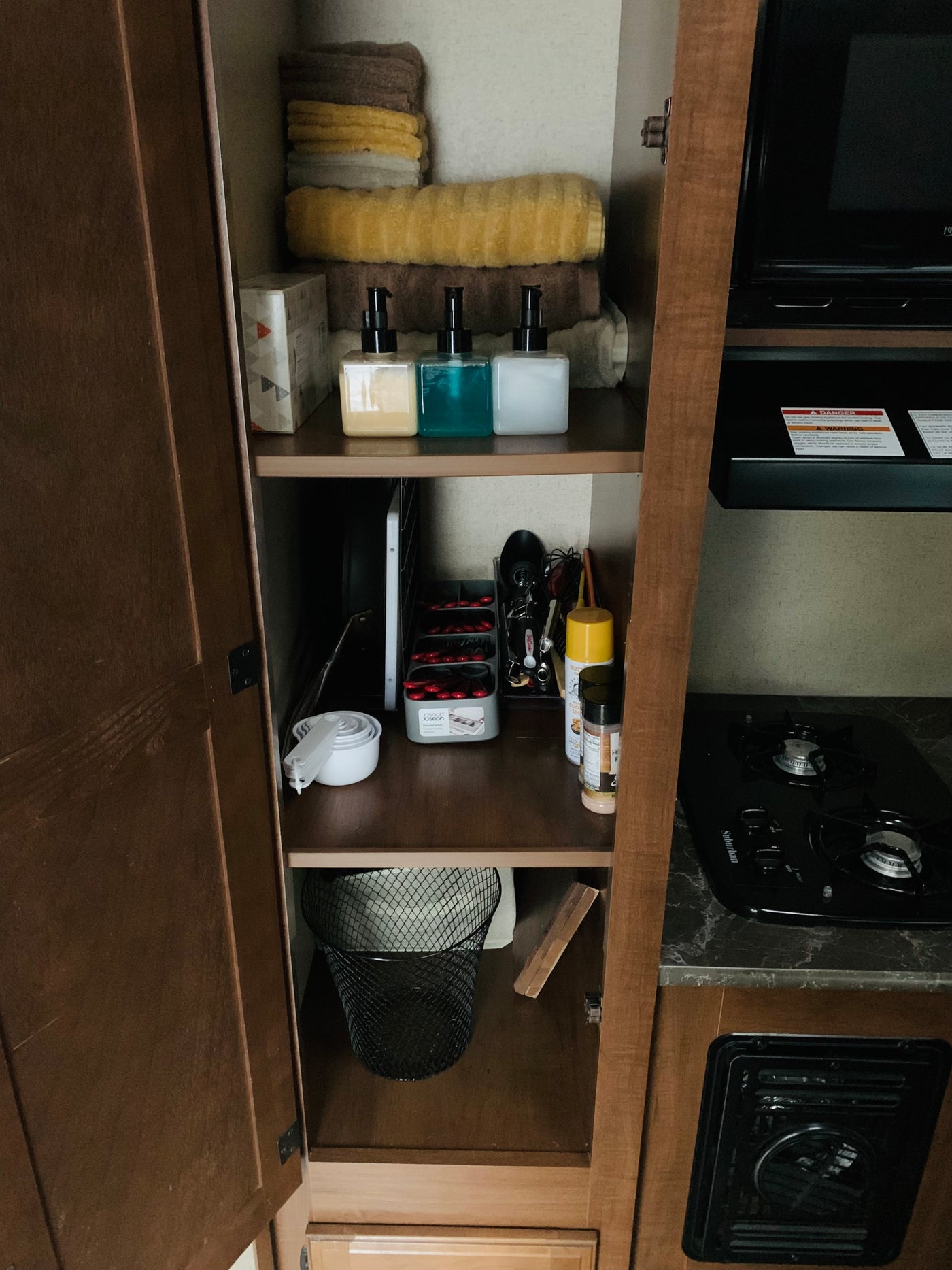 RV rental storage: organized cabinet shelves with folded towels, pump bottles, kitchen utensils, spices, and a waste bin. — photo 3
