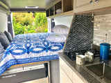 Inside a modern RV rental: comfy bed, compact kitchen with stovetop & sink, and serene outdoor views. Dometic fridge visible.