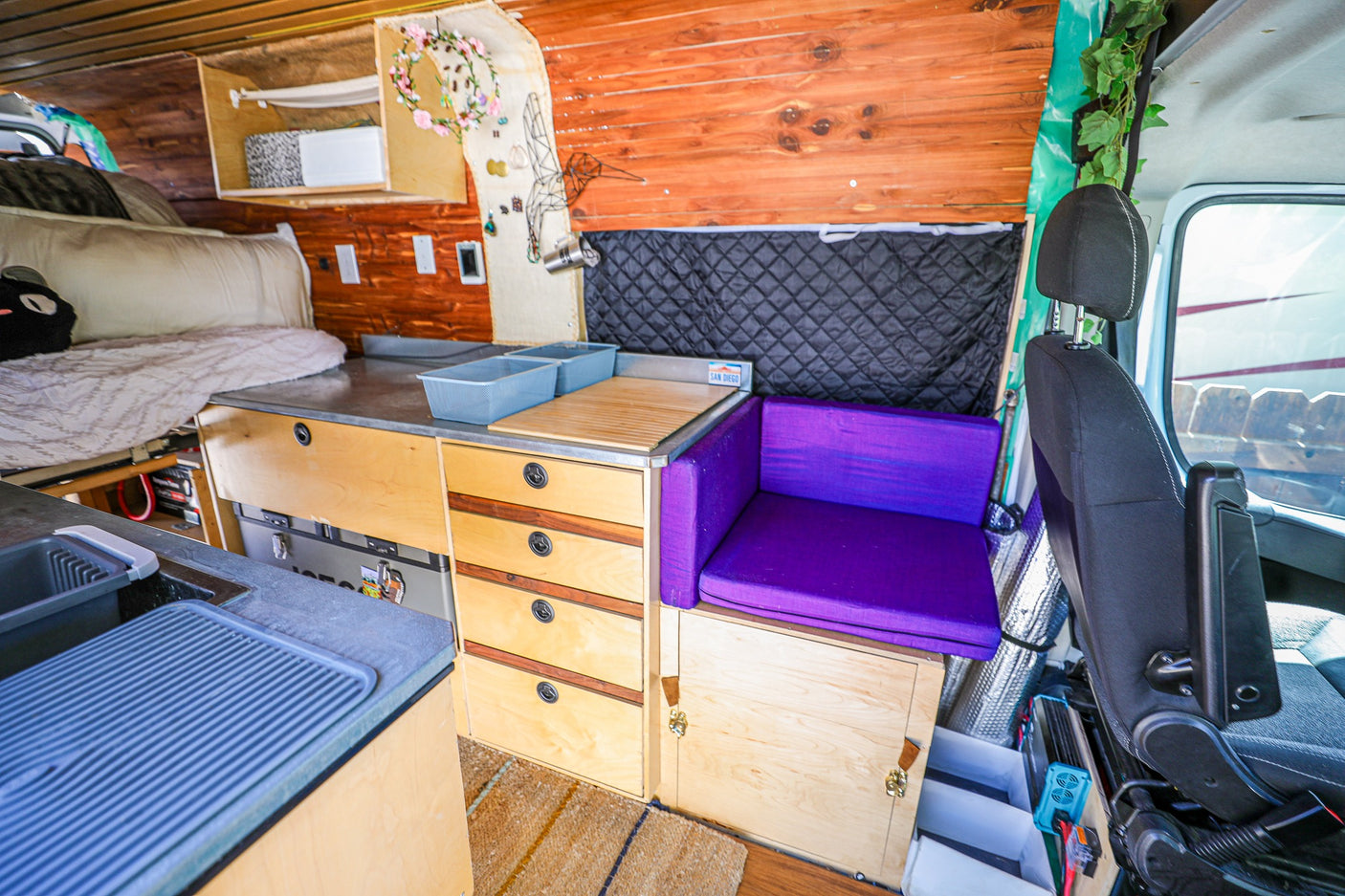 Inside an RV rental: a compact camper van interior featuring a bed, kitchenette, and purple bench seating for adventurers.