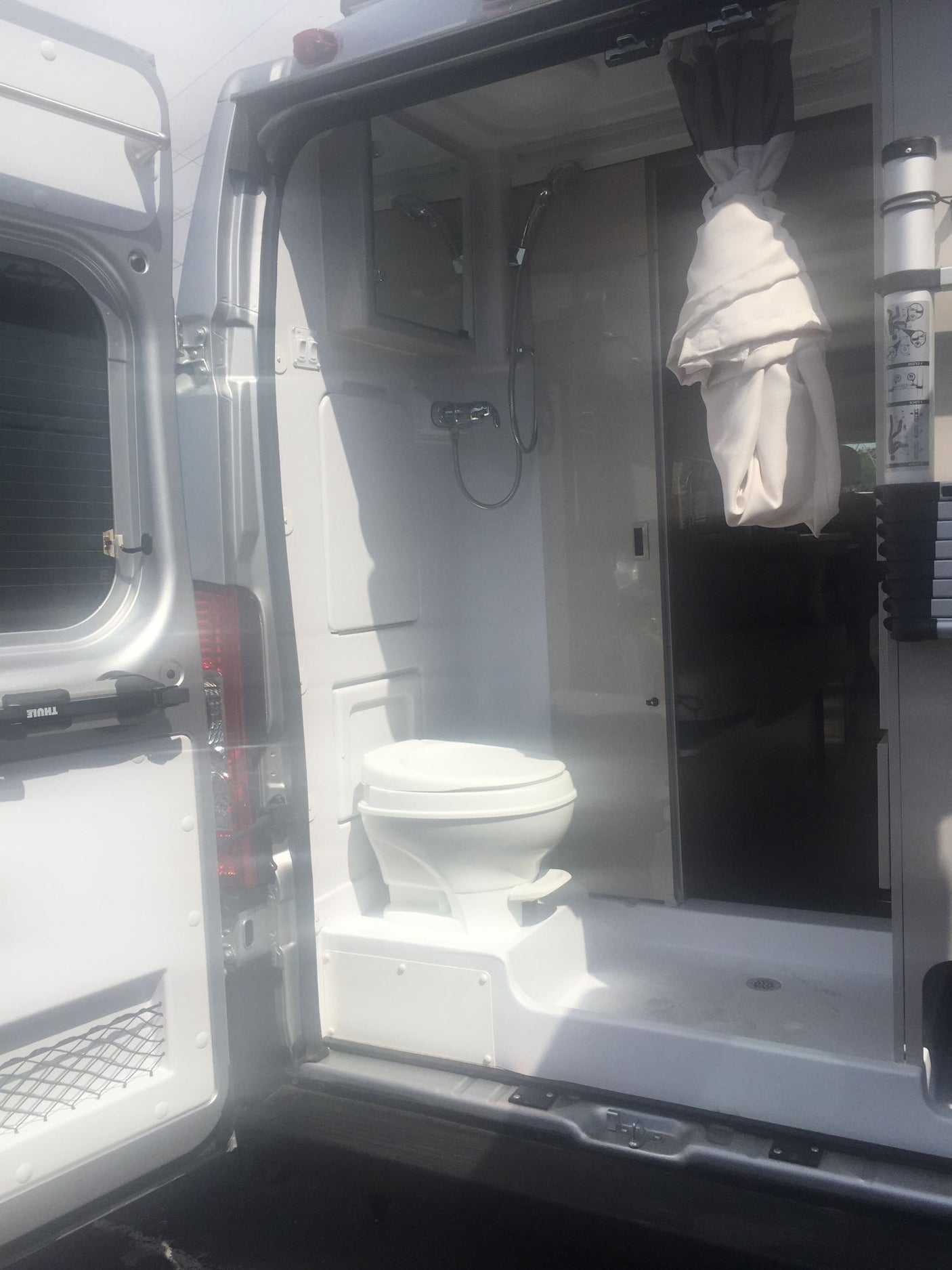 RV rental: a bright, compact bathroom featuring a white toilet, showerhead, and pull-back curtain. Perfect for mobile living.