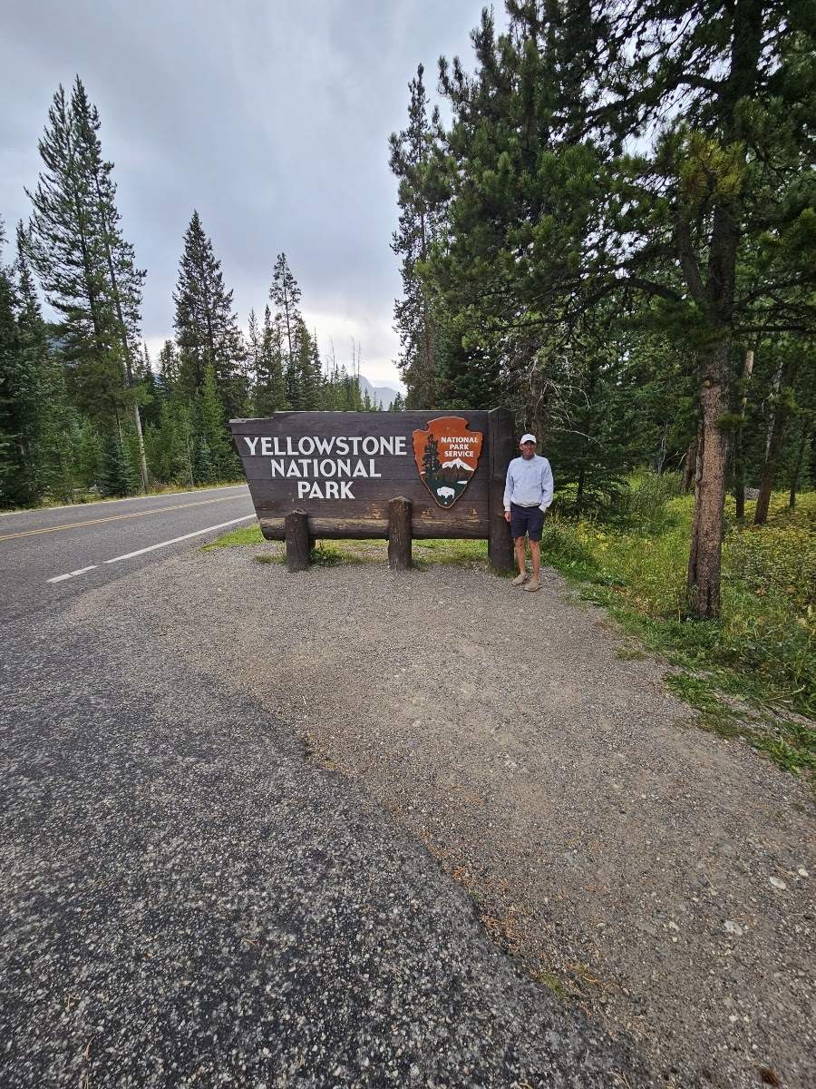 Man by Yellowstone National Park sign. Your RV rental adventure starts at this iconic entrance to explore nature!