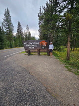 Man by Yellowstone National Park sign. Your RV rental adventure starts at this iconic entrance to explore nature!