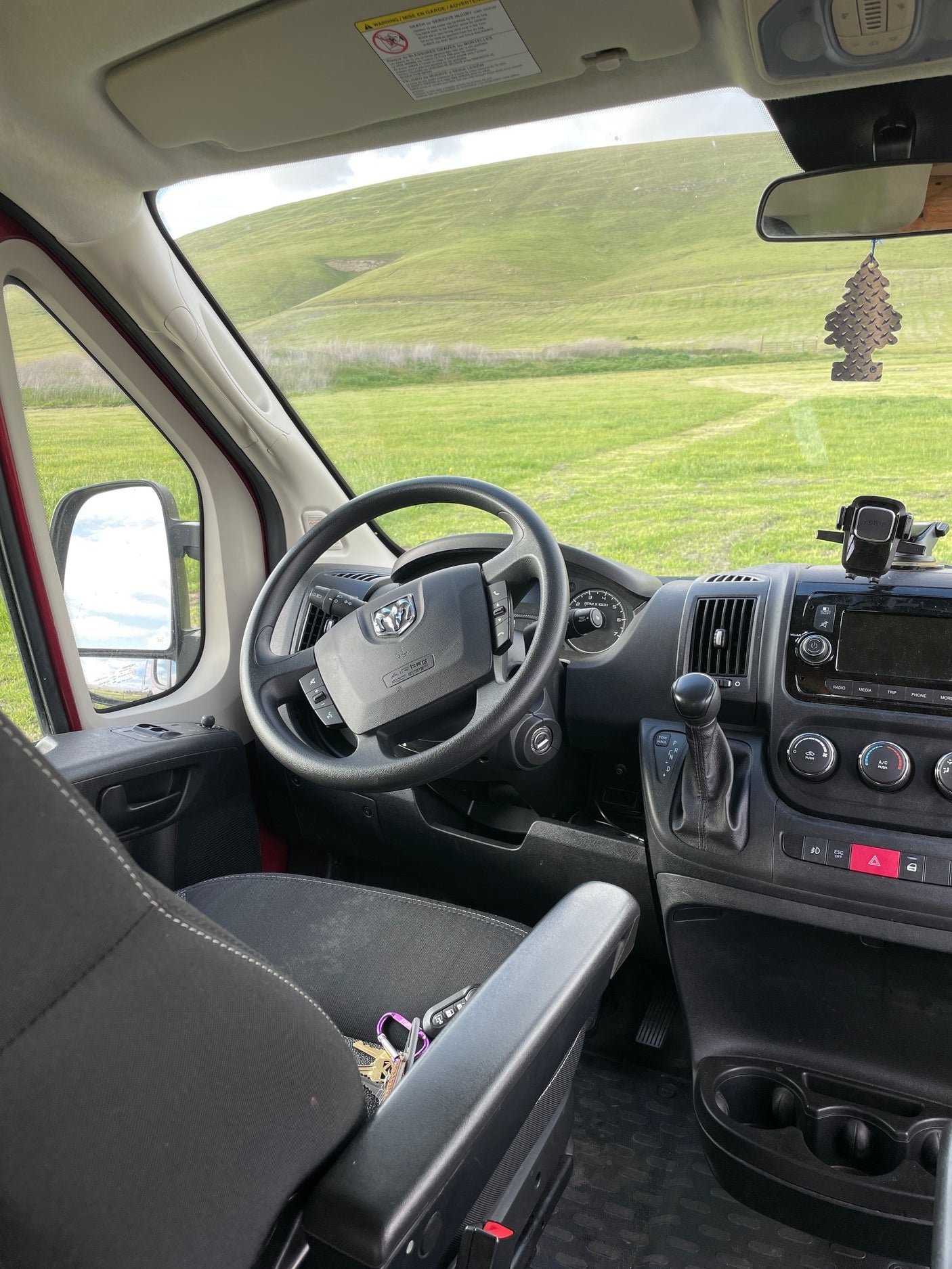 Driver's perspective inside an RV rental, showcasing the dashboard and a scenic view of rolling green hills.