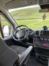 Driver's perspective inside an RV rental, showcasing the dashboard and a scenic view of rolling green hills.