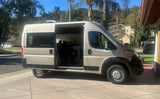 A modern beige camper van for rv rental, parked with its side door open, revealing a custom interior with seating and a kitchen.