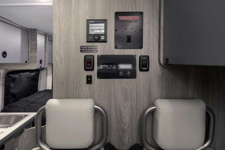 RV rental: Interior control panel for heating, solar power, and various systems, seen above cozy seating.