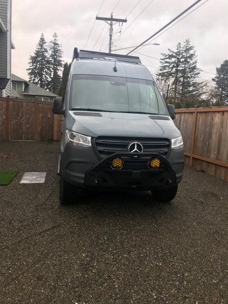 Grey Mercedes-Benz Sprinter camper van with custom bumper & roof light bar. Perfect for an RV rental adventure on a gravel drive.
