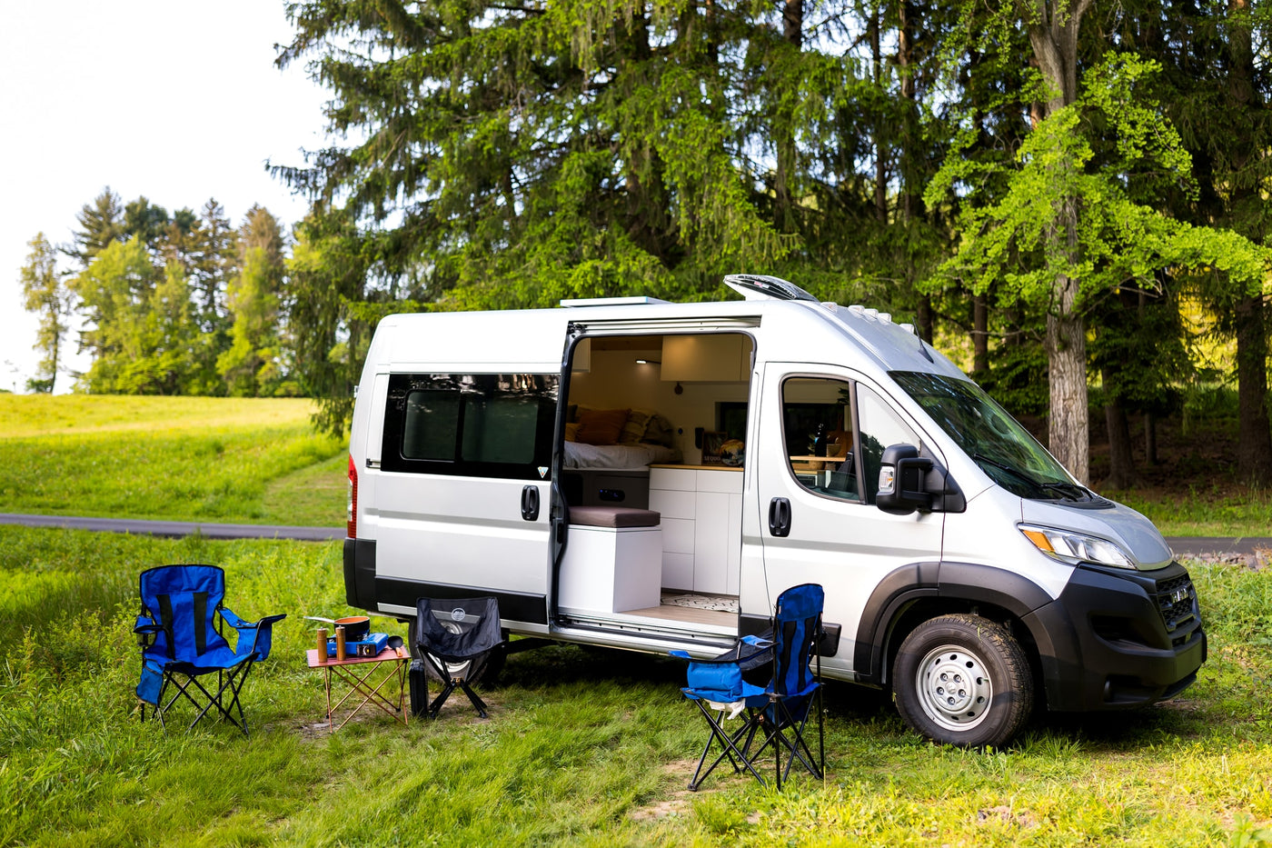 Silver camper van RV rental parked in grass, side door open. Camping chairs & cook set up outside for an outdoor adventure. — photo 3
